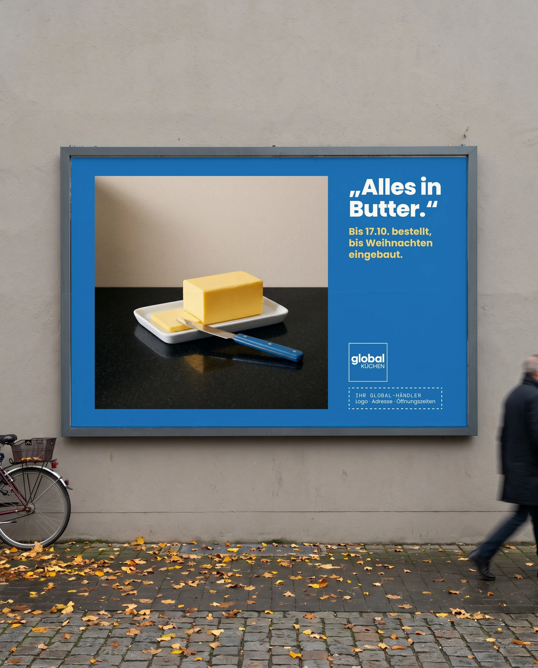 Global Küchen 18/1 billboard on a town wall in autumn: a block of butter on black stone, headline „Alles in Butter.“